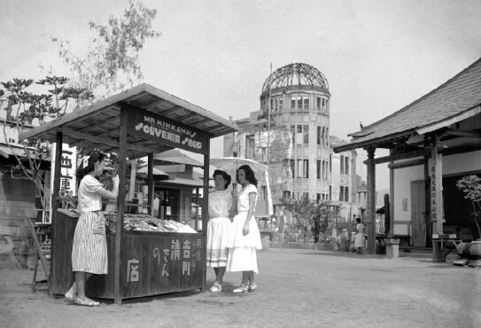 1951年8月3日，距離廣島原子彈爆炸已經過去了6年，街頭紀念品攤點背后是被原子彈破壞的遺跡，攤主也在那次爆炸中受傷。
