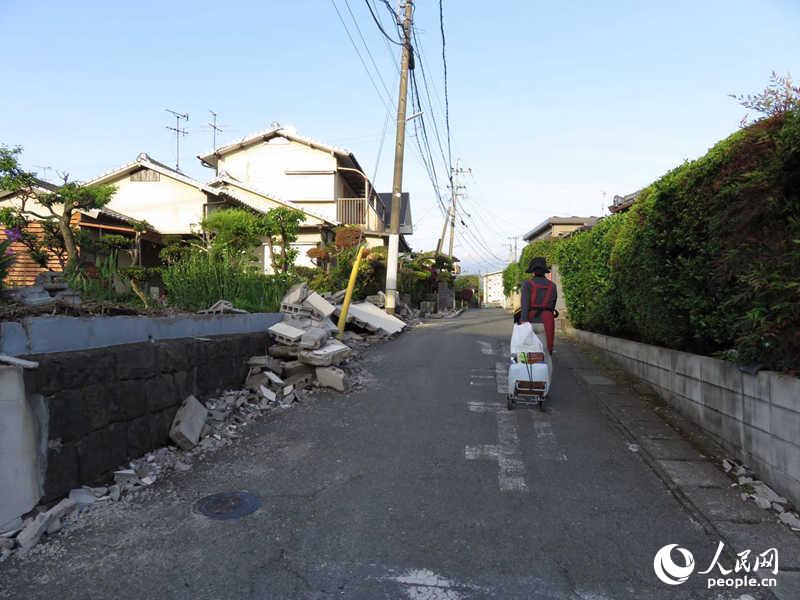 4月22日，益城町的一名老年人領取完救災物資，經過倒塌的民宅