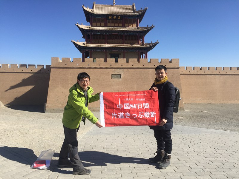2月18日，入船亭游京（右）与许飞（左）在甘肃嘉峪关，与日文旗帜合影留念（许飞供图）