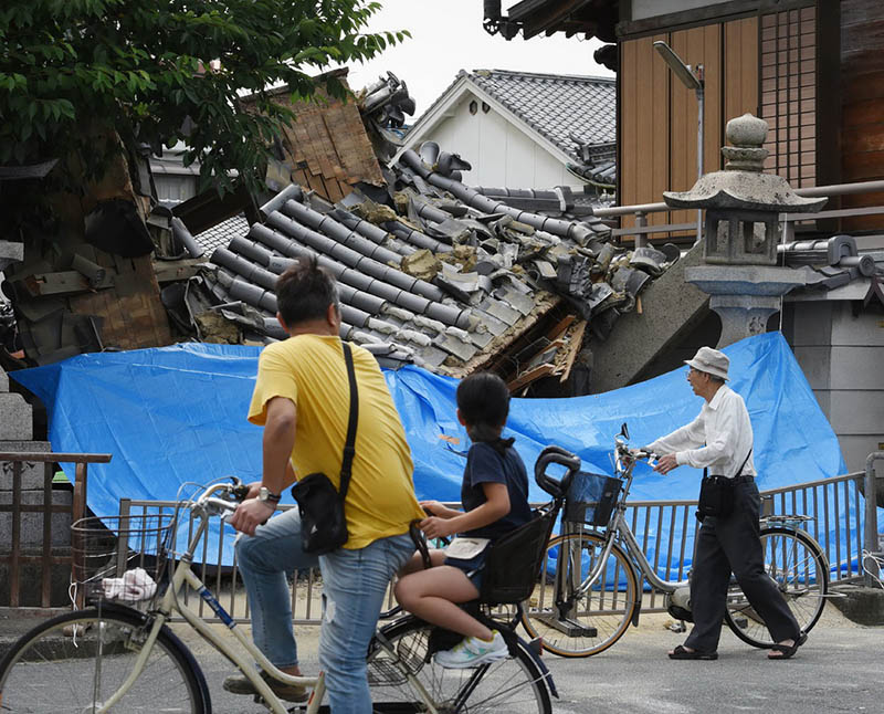 6月18日，在日本大阪，行人望向倒塌的房屋。新華社/法新