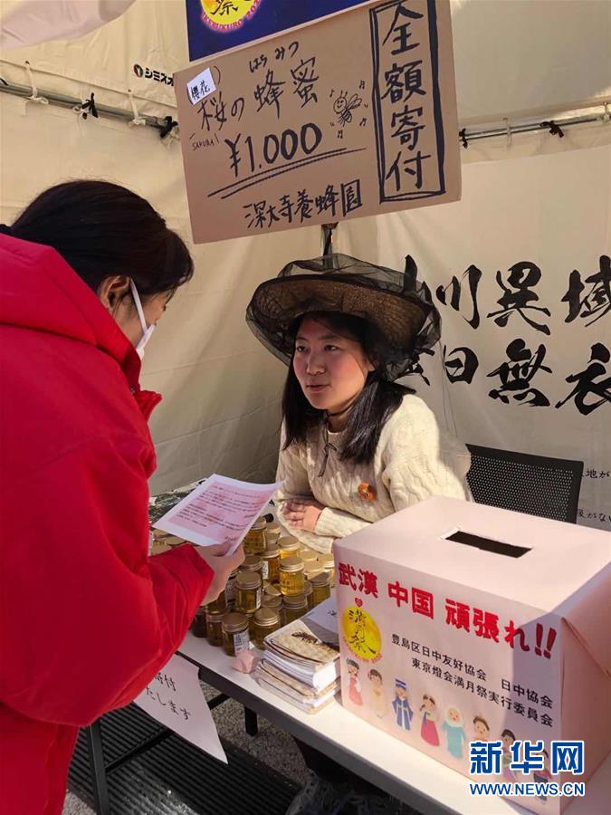 2月8日，在日本東京池袋的元宵節慶祝活動現場，“為中國武漢加油攤位”的工作人員（右）向市民介紹情況。該攤位為中國抗擊新冠肺炎疫情向人們募捐，並將銷售蜂蜜所得全部捐出。新華社發（劉莉生 攝）